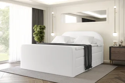 A white boxspring bed with a headboard is shown in a bedroom setting.