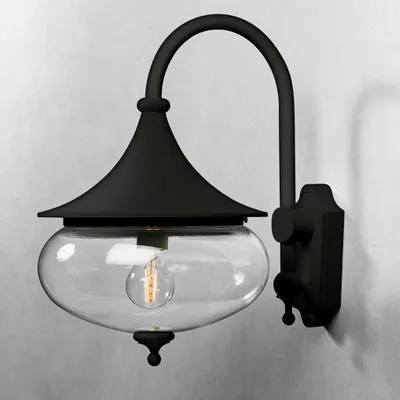 A black outdoor wall light with a clear glass shade is mounted on a light gray wall.