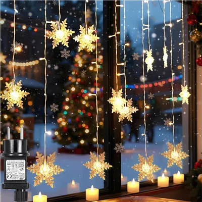 Christmas lights shaped like snowflakes hanging in a window with a Christmas tree visible in the background.