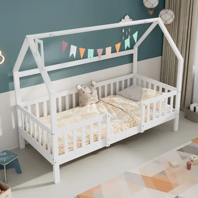 A white wooden house-shaped bed for children, decorated with a colorful banner and a stuffed animal.