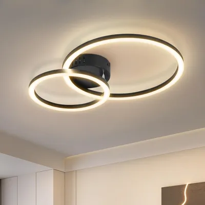 A modern ceiling light with two interlocking rings, illuminated with warm white LED light, mounted on a white ceiling.