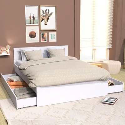 A bedroom scene with a white bed frame and drawers, featuring a light-colored duvet and pillows. The wall behind the bed is decorated with framed artwork.