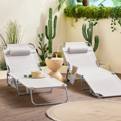 Two beige lounge chairs are set up on a wooden deck, surrounded by potted plants and cacti, creating a relaxed outdoor oasis.