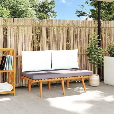 A wooden garden bench with cushions is placed on a patio in front of a bamboo fence.