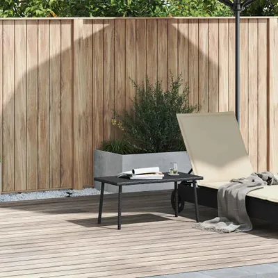 A patio scene with a wooden fence, a planter with greenery, a lounge chair, and a small coffee table.