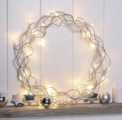 A metallic wreath with LED lights and decorative ornaments on a wooden shelf.