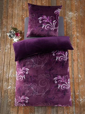 A flat lay of a purple duvet cover and pillow with a floral pattern, set against a rustic wooden background with scattered white elements resembling snow.