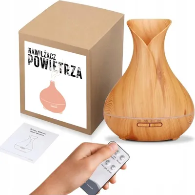 A product shot of an aroma diffuser, its packaging, a manual, and a remote control, with a hand holding the remote.