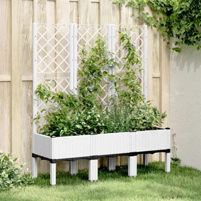 A white raised garden bed with a lattice back and plants, positioned against a wooden fence.