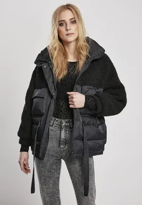 A woman is modeling a black puffer jacket with sherpa accents and gray acid-wash jeans.