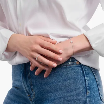 A person wearing a white shirt and blue jeans, showing off a ring and a bracelet.