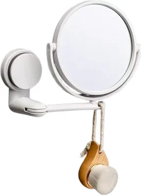 A white makeup mirror with a suction cup mount and a wooden facial brush hanging from it.