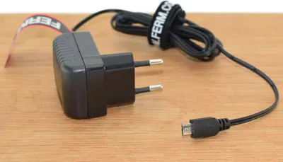 A black power adapter with a USB micro B cable is placed on a wooden surface.