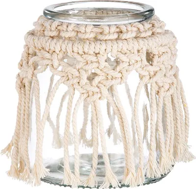 A glass jar decorated with a cream-colored macrame cover and fringe.