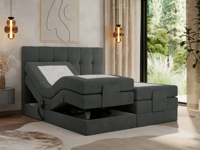 A bedroom scene featuring a dark gray upholstered boxspring bed with an adjustable mattress and topper, set against a textured wall with artwork and a large window overlooking greenery.