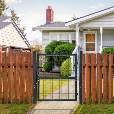 A metal garden gate is shown in front of a house, with a wooden fence on either side.