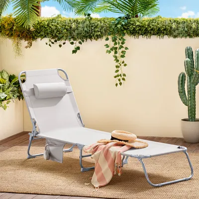 A beige lounge chair with a striped blanket and straw hat on a patio with plants and a cactus.