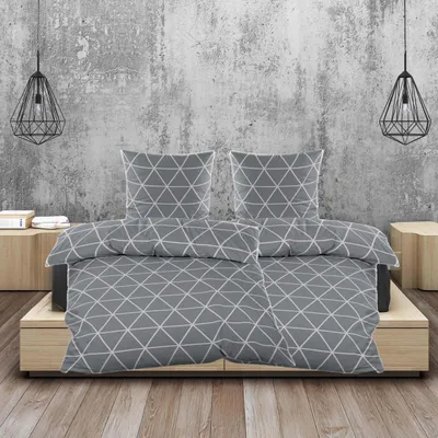 A bed with grey and white geometric patterned bedding is shown against a textured concrete wall.