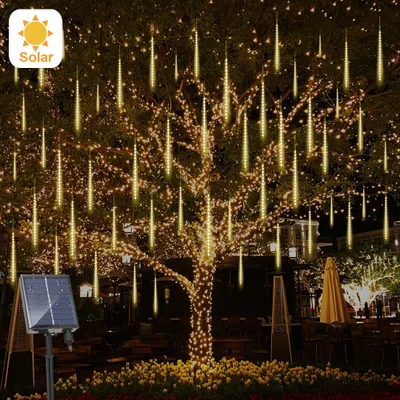 A tree decorated with solar-powered meteor shower string lights at night, with a solar panel visible in the foreground.