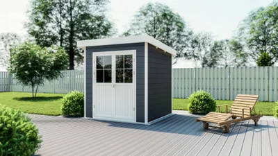 A dark gray garden shed with white double doors sits on a gray deck in a backyard setting. A wooden lounge chair is placed to the right of the shed, and green bushes and a fence are visible in the background.