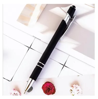 A black ballpoint pen with silver accents is laid diagonally on a white surface with some drawn lines and two small dried flowers.