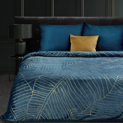 A close-up view of a bed with a dark blue blanket featuring a gold leaf pattern, and two dark blue pillows with a gold accent pillow.