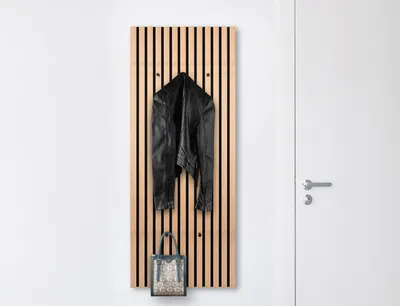 A wooden slat panel with a black leather jacket and a patterned bag hanging on it, next to a white door.