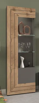 A tall, narrow vitrine cabinet with a wood-effect frame and gray front panels, displaying decorative items and glassware.