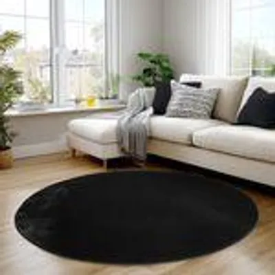 A black round rug in a living room setting with a sectional sofa and plants.