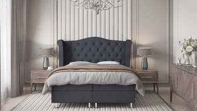 A bedroom scene featuring a large boxspring bed with a tufted headboard, bedside tables with lamps, and a dresser with flowers.