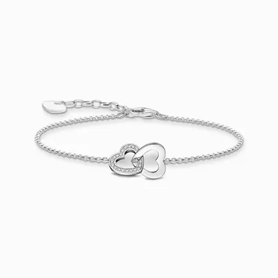 A silver bracelet with two intertwined heart charms, one of which is adorned with small clear stones.