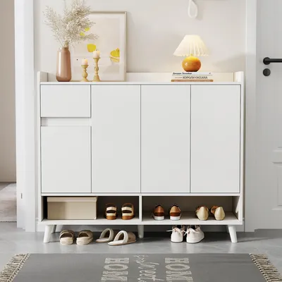 A white shoe cabinet with several compartments and shelves, displaying various shoes and a decorative box. The cabinet is placed in a hallway or entryway, with a rug in front of it.