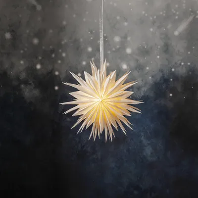 A white paper star lantern hangs against a dark, speckled background that resembles a night sky with faint stars and a comet.