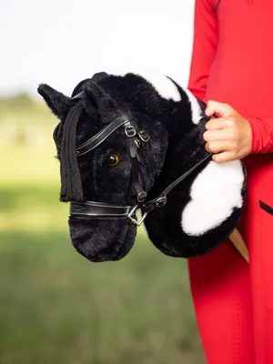 A person in a red outfit holds a black and white hobby horse in a grassy outdoor setting.