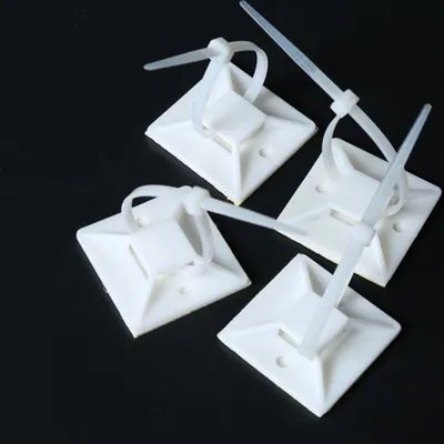 Four white cable tie mounts with cable ties attached, arranged on a black surface.