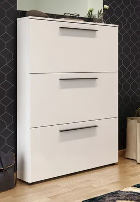 A white shoe cabinet with three drawers against a black geometric patterned wall.