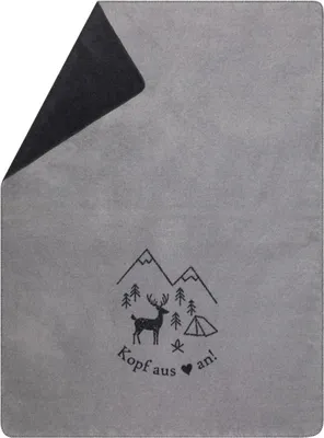 A folded gray blanket with a black graphic design of mountains, trees, a deer, and a tent, with text below.