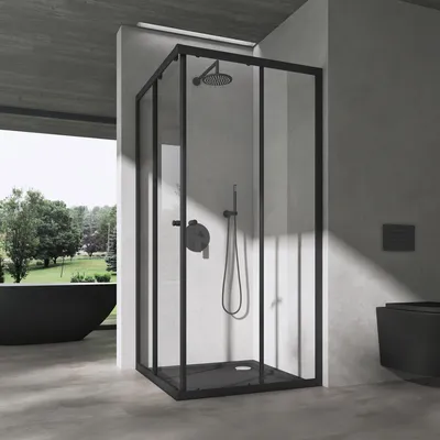 A modern bathroom with a black framed shower enclosure, a black bathtub, and a black toilet, set against a concrete wall and floor, with a view of greenery outside.