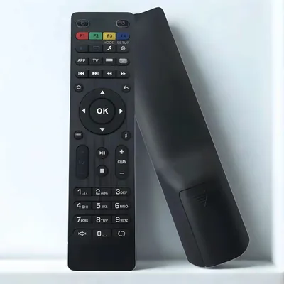 A black remote control is leaning against a white surface.
