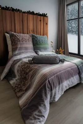 A cozy bedroom scene with a bed dressed in patterned bedding, a window showing a snowy landscape, and decorative lights.
