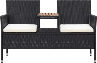 A black rattan garden bench with white cushions and a small wooden table in the center.