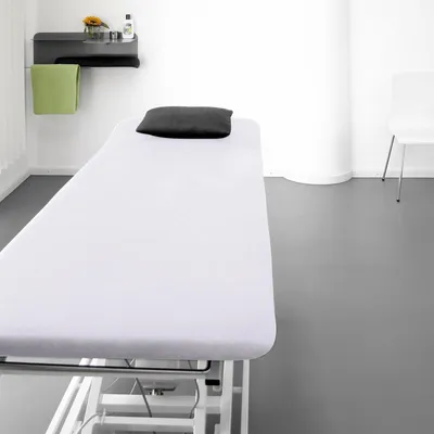 A clean, minimalist room with a treatment table, shelf, and chair.