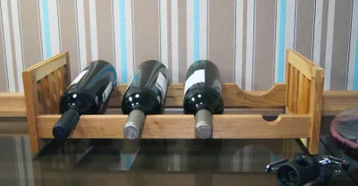 A wooden wine rack holding three bottles of wine, placed on a reflective surface with a striped background.