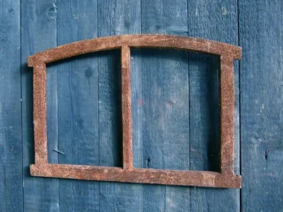 A rusty metal window frame is mounted on a weathered blue wooden wall.