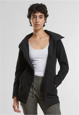 A woman wearing a black jacket and white tank top, standing against a white background.