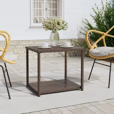 A brown poly rattan side table with two cups and a vase of flowers on top, placed on a patio next to two chairs.