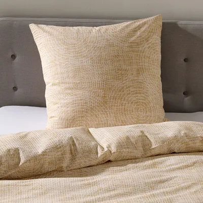 A close-up view of a bed with beige seersucker bedding and a pillow.
