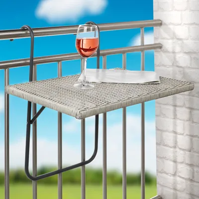 A small folding table attached to a balcony railing, with a glass of rose wine and a folded napkin on it.