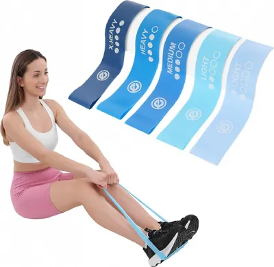 A woman is sitting on the floor and using a light blue resistance band around her feet for exercise.