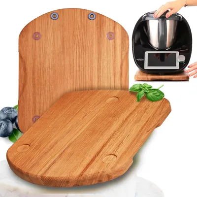 Two wooden cutting boards are shown, one in the foreground and one behind it. A black kitchen appliance with a silver bowl is on the back cutting board, and a hand is reaching towards it. Blueberries and a sprig of basil are also visible.